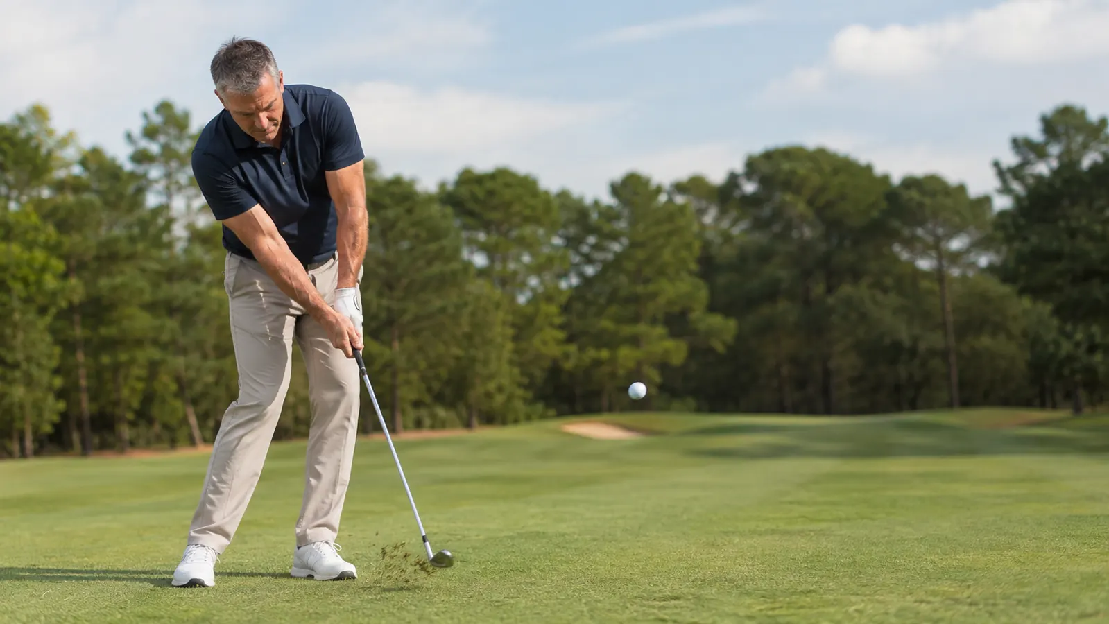 Close-up of a wedge striking through a pitch shot, a small divot kicking forward and the ball launching off the face
