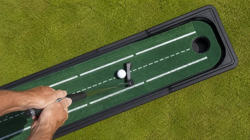 A close overhead shot of a golf ball resting on the striped end of a putting mat near the target cup